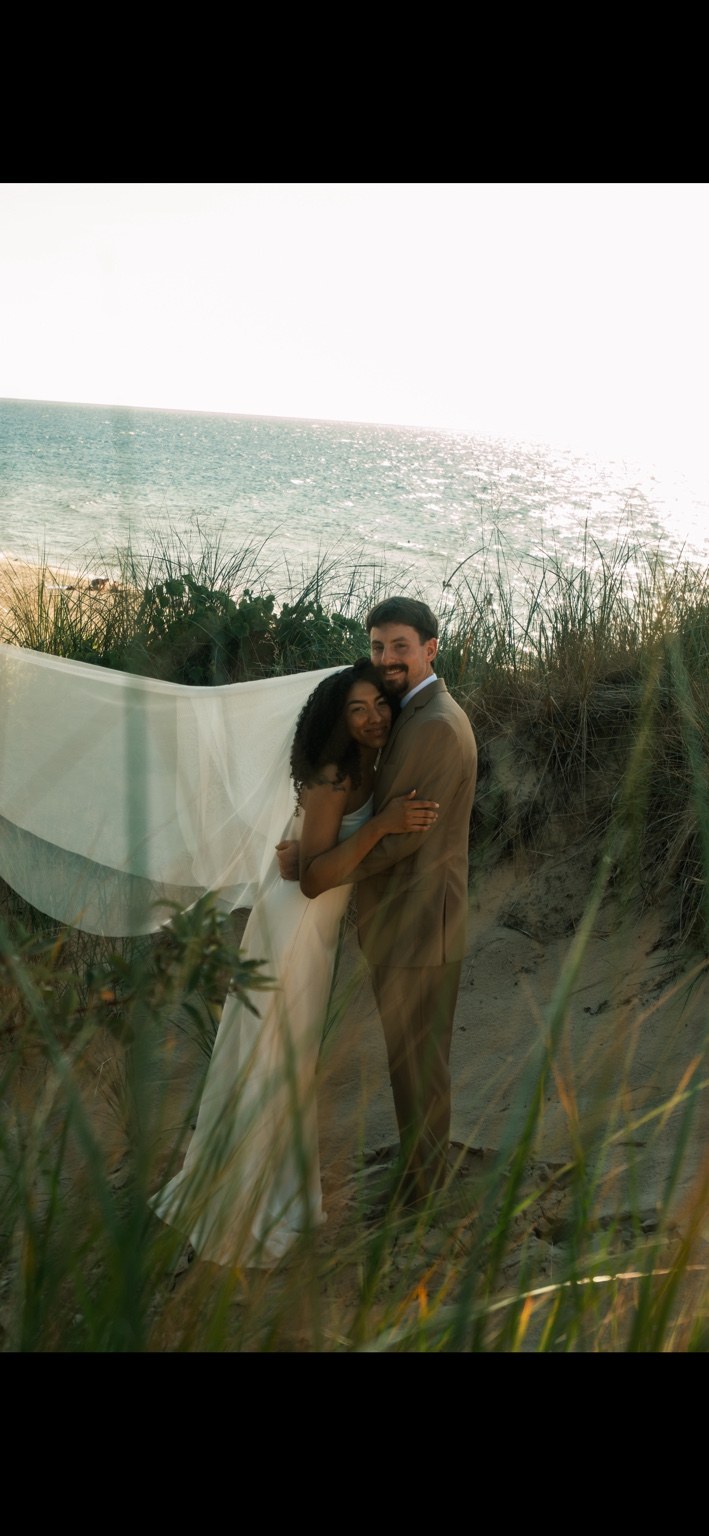 Newlywed couple embracing in beach grass by the water