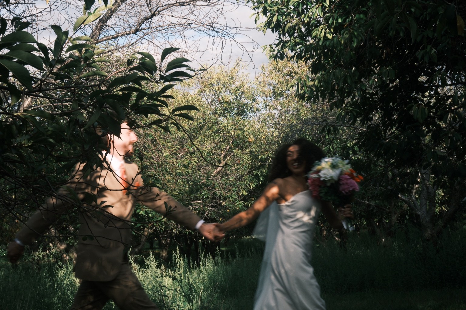Newlyweds running hand in hand through trees