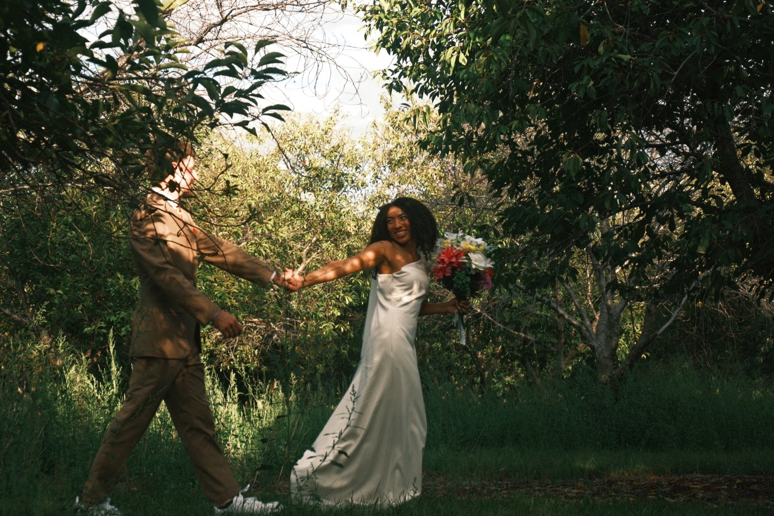 Newlyweds laughing while holding hands in an orchard